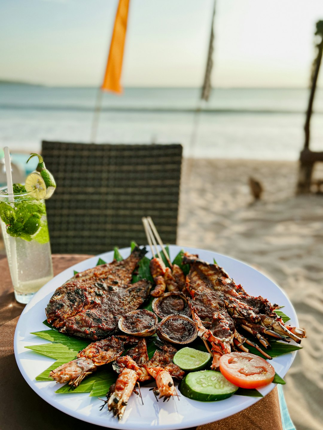 Seafood platter with grilled fish and shellfish on sandy beach.