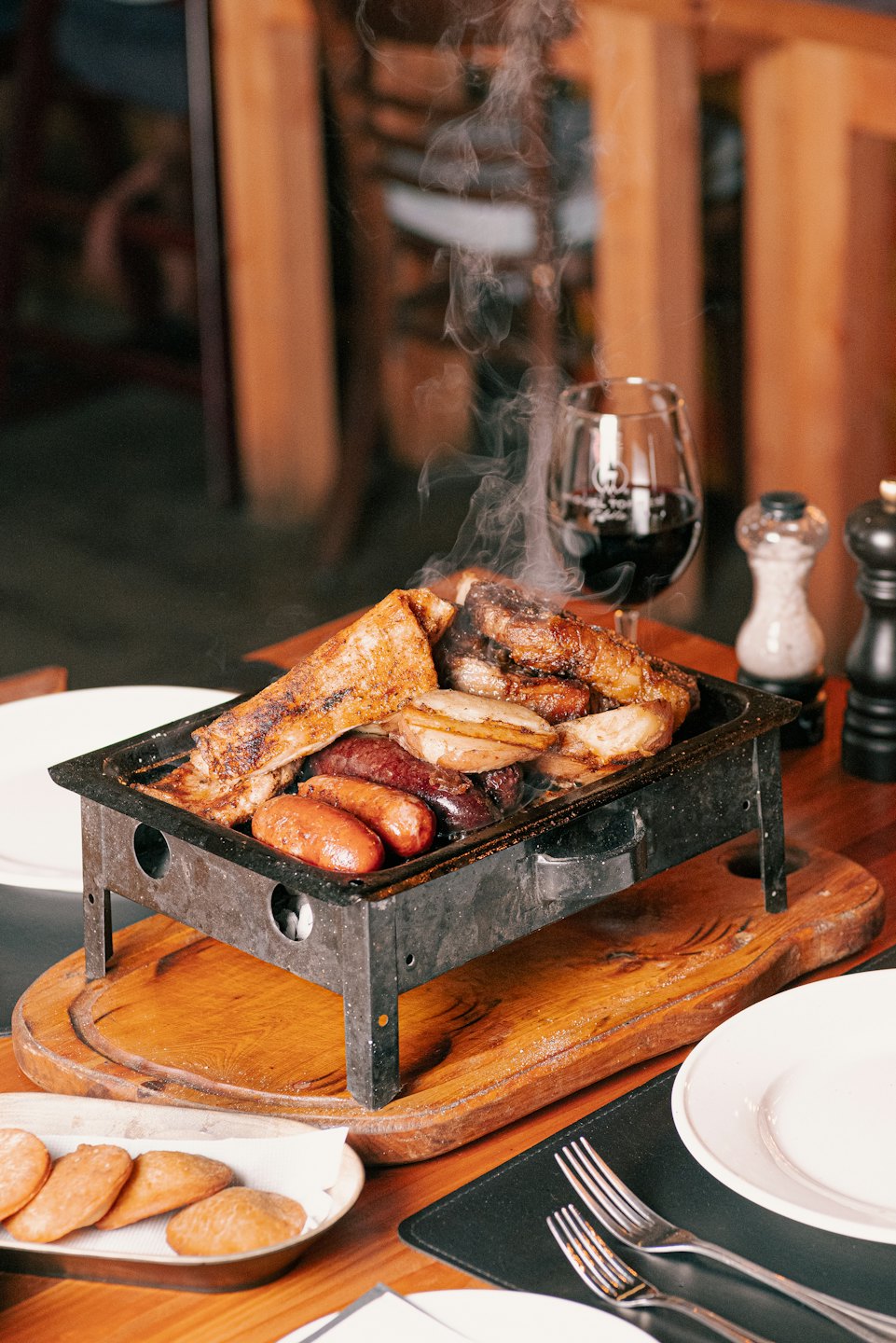 Steaming grilled meats and sausages served on a metal tray.